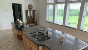 A kitchen with a granite countertop, two sinks, wooden cabinets, and a window with blinds. - Private,Spacious House near Howes Cavern (Carisle)