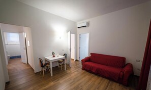 A room with a red sofa, a white table with chairs, and an air conditioning unit on the wall.