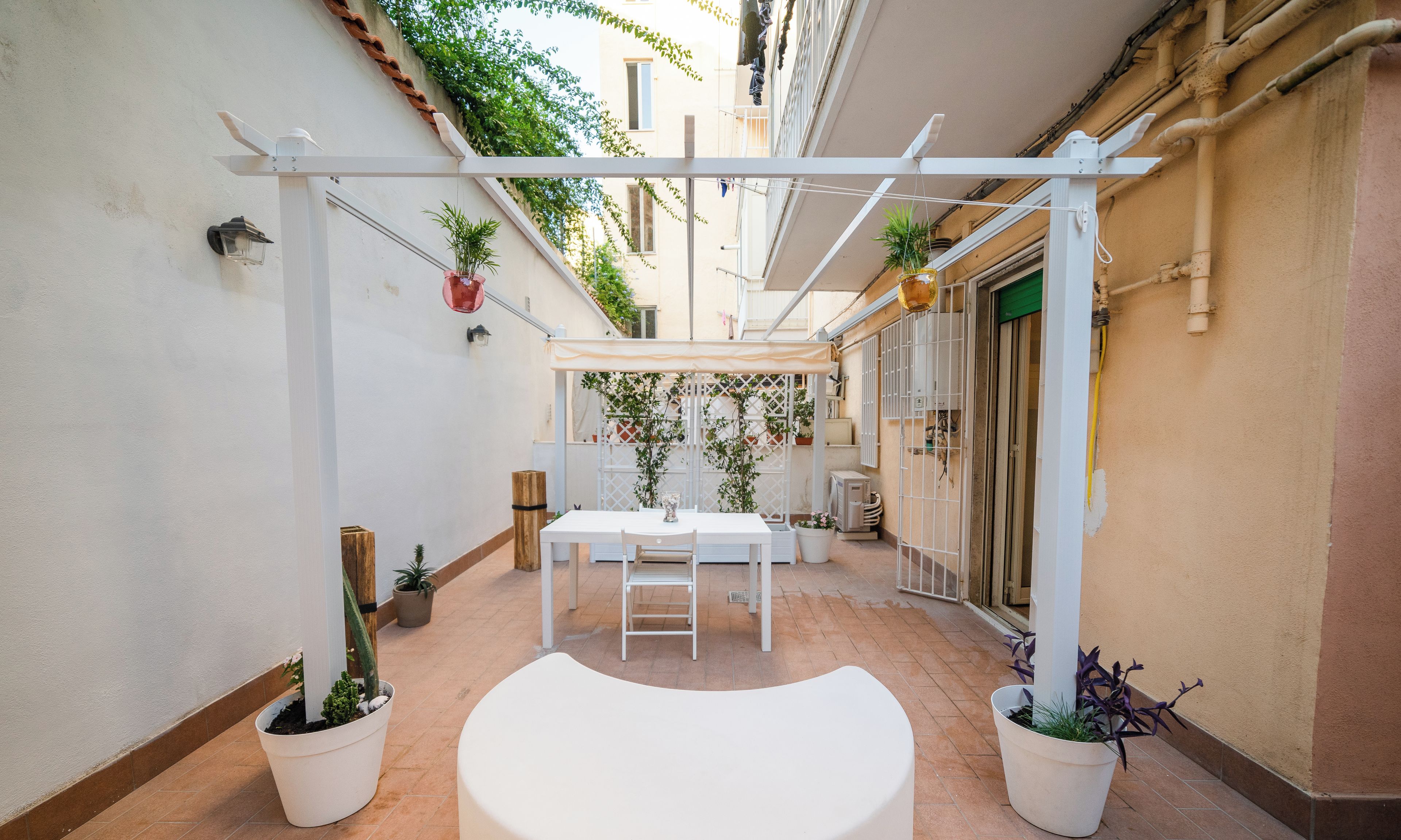 A covered patio area with a white table and chairs, potted plants, and a white bench.