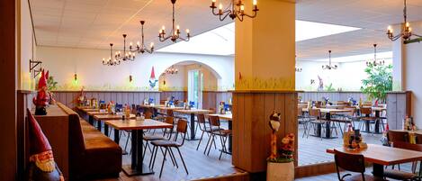Un restaurante espacioso con techos altos, varios candelabros, mesas y sillas de madera, y estatuas decorativas de gnomos.