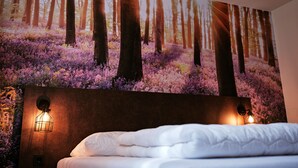 Quarto com um grande mural temático de floresta, uma cama bem arrumada e duas luminárias fixadas na parede.