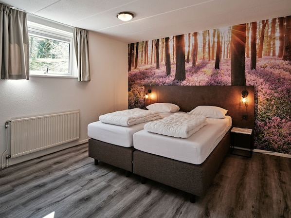 Un dormitorio con cama doble, radiador, ventana con cortinas y un mural temático de bosque.