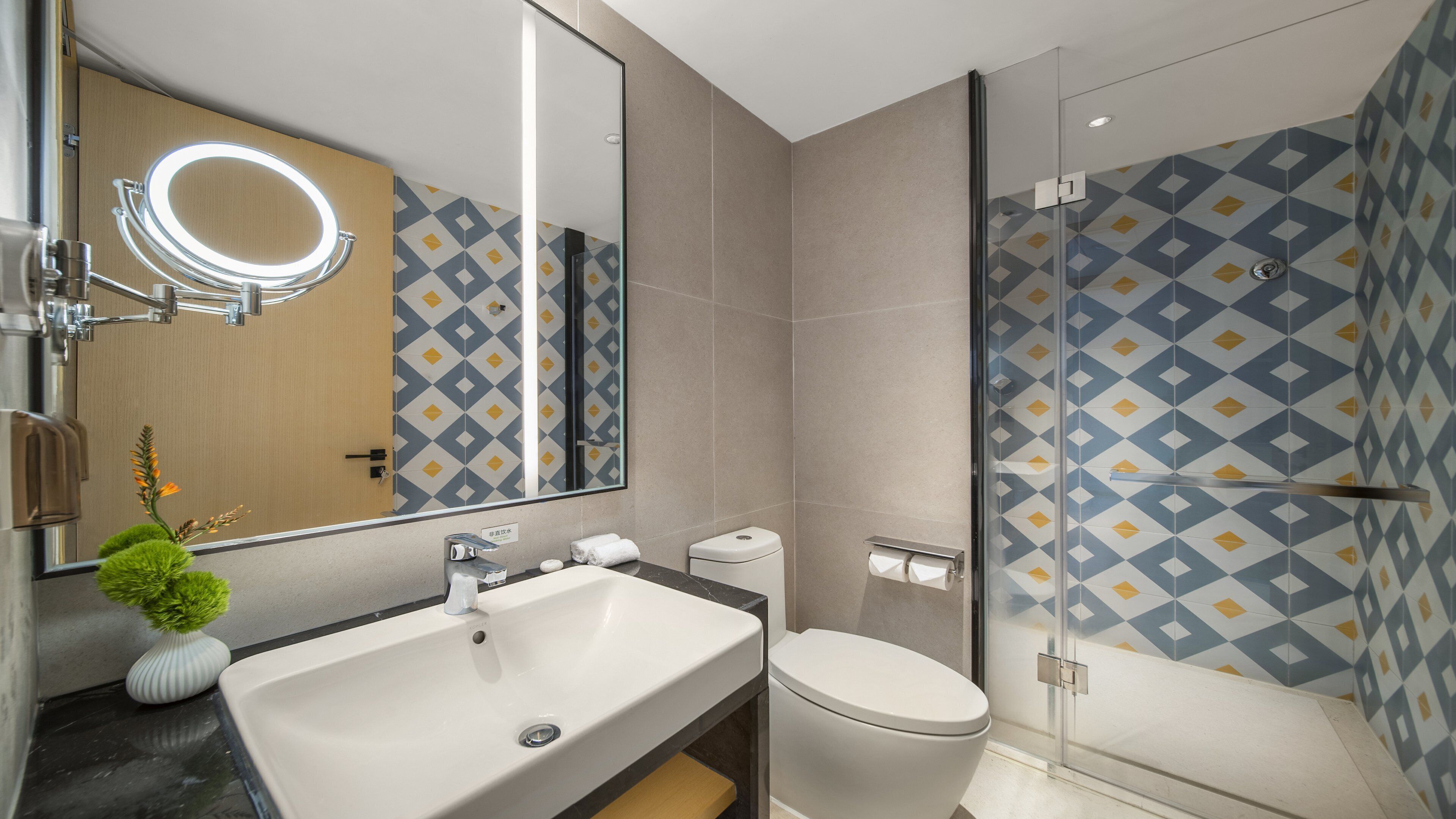 A modern bathroom with a large mirror, sink, toilet, and glass shower enclosure.