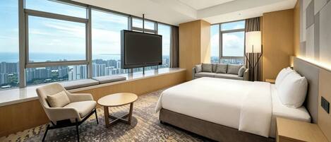 A hotel room with a large bed, a sofa, a TV, and a view of the city.