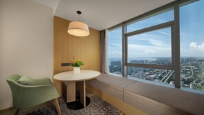 Habitación de hotel con un ventanal grande, una mesa redonda con un florero y una silla verde, además de una lámpara en el techo.