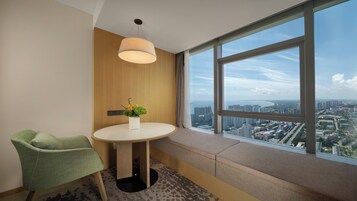 Habitación de hotel con un ventanal grande, una mesa redonda con un florero y una silla verde, además de una lámpara en el techo.
