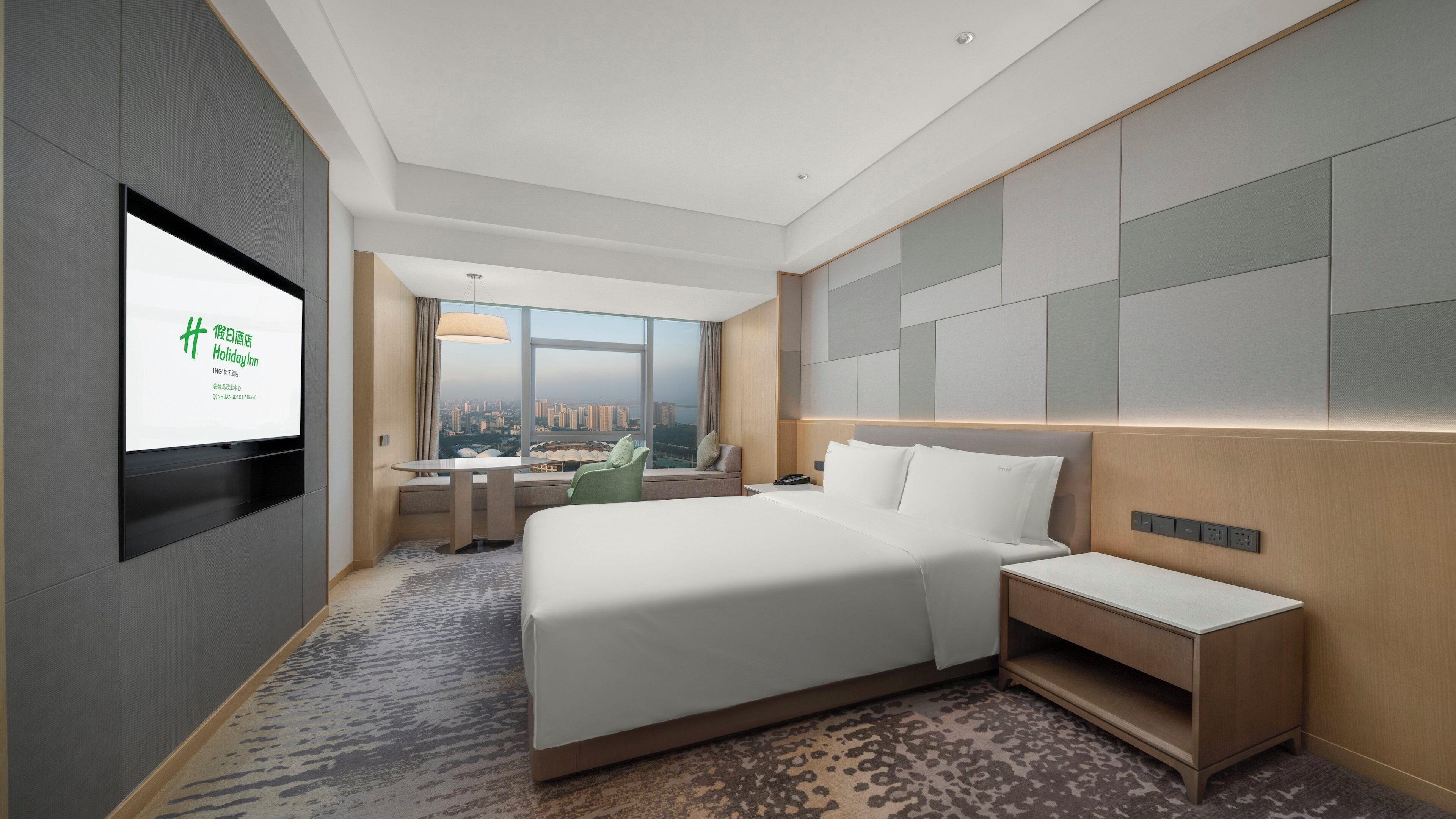 A modern hotel room with a large bed, a desk, and a view of the cityscape.