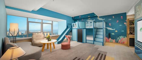 A modern living room with a city view, a sofa, a coffee table, a lamp, a slide, and a play area with a blue theme.