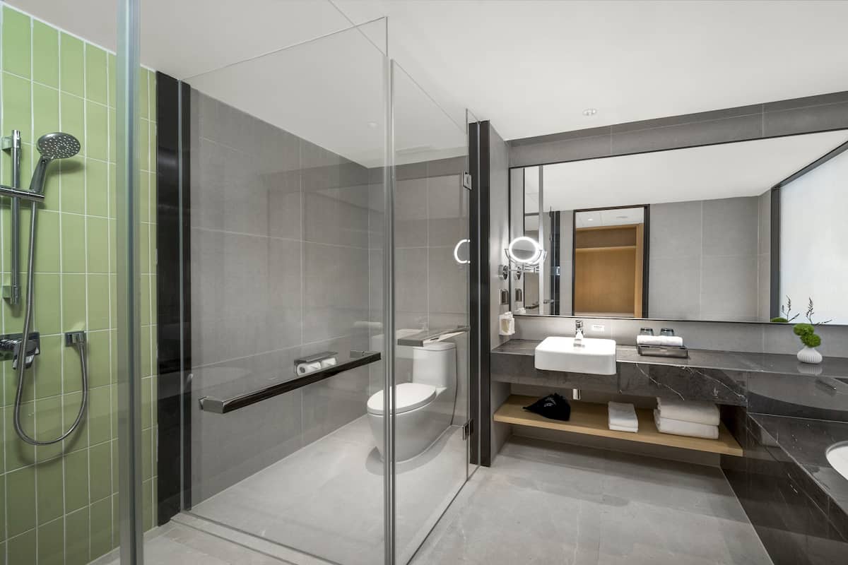 Une salle de bain moderne dotée d’une douche à parois de verre, d’un grand miroir et d’un meuble-lavabo avec un évier et un porte-serviettes.