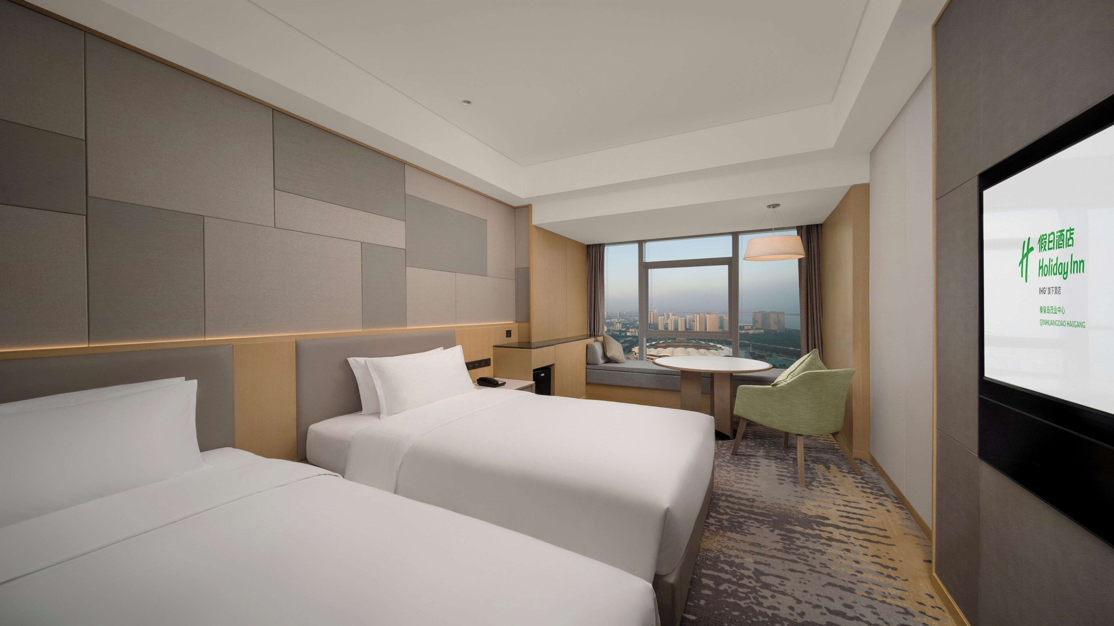 A hotel room with two beds, a desk, a chair, and a large window offering a city view.