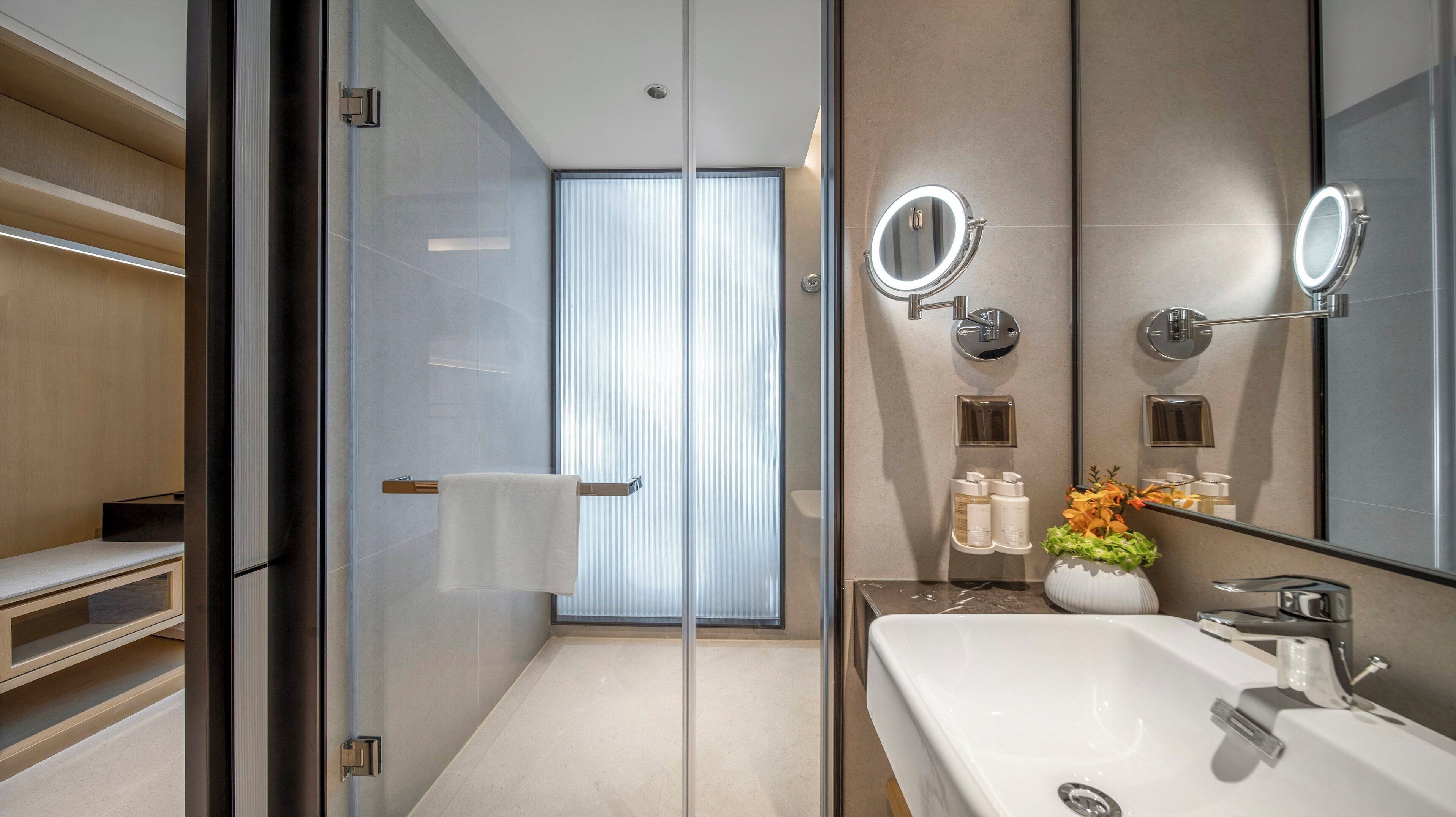 A modern bathroom with a glass shower enclosure, a large mirror, a white sink, and a towel rack.