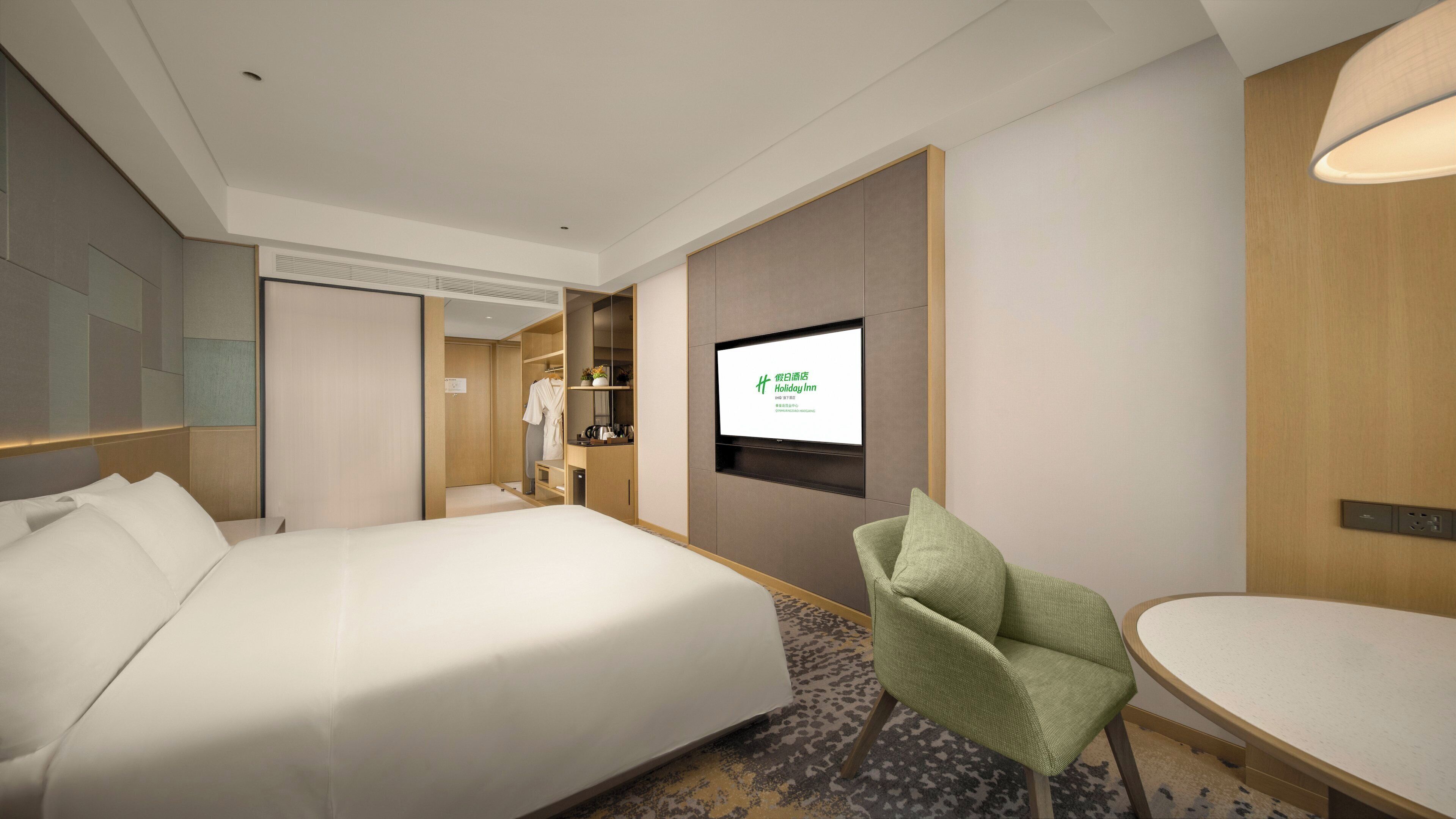 A hotel room with a bed, a TV mounted on the wall, a chair, and a small table.