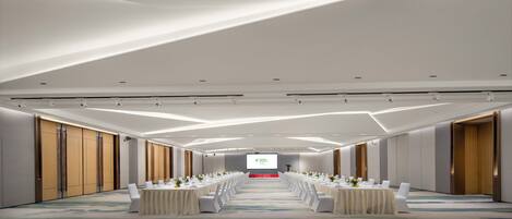 Un salón de conferencias con una larga mesa dispuesta para una reunión, equipado con una pantalla de proyector al frente.
