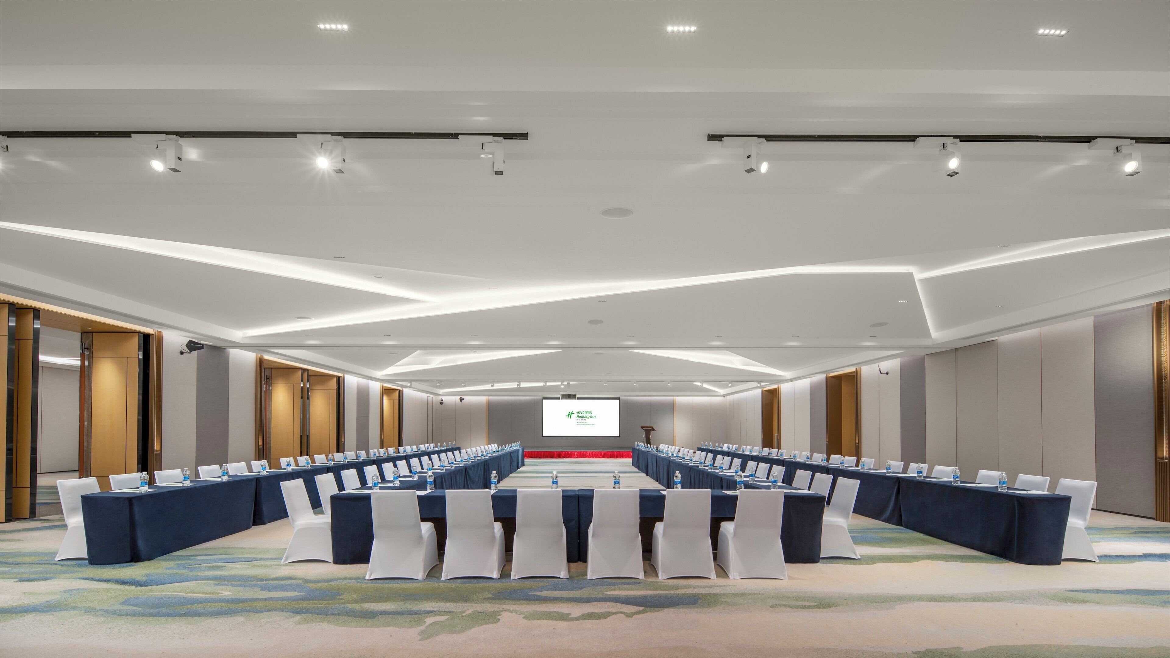 Un salón de conferencias con una larga mesa, varias sillas y una pantalla de proyección.
