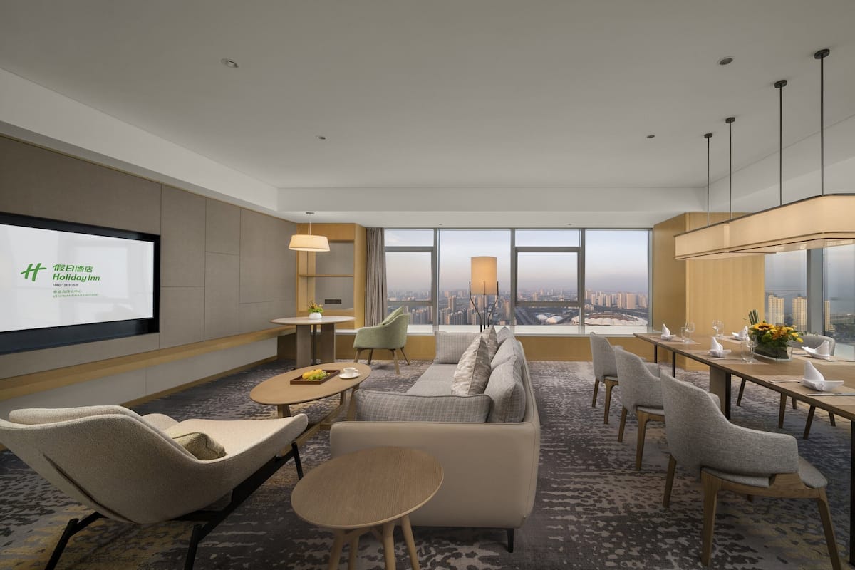 Une chambre d’hôtel moderne offrant une vue imprenable sur la ville, un coin salon confortable et une table à manger dressée pour deux personnes.