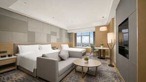 A modern hotel room with a large bed, a sofa, a small table with a plant, a TV, and a city view.