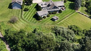 An aerial view of a large estate with multiple buildings, including a main house with a large porch and several smaller structures. There are well-maintained lawns and a lake in the background. - Secluded Lakefront Chalet  (Grass Lake)