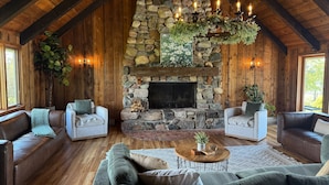 A cozy living room with a stone fireplace, wooden beams, and comfortable seating. - Secluded Lakefront Chalet  (Grass Lake)