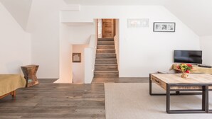 A modern living room with a wooden staircase, a sofa, a coffee table, and a TV.