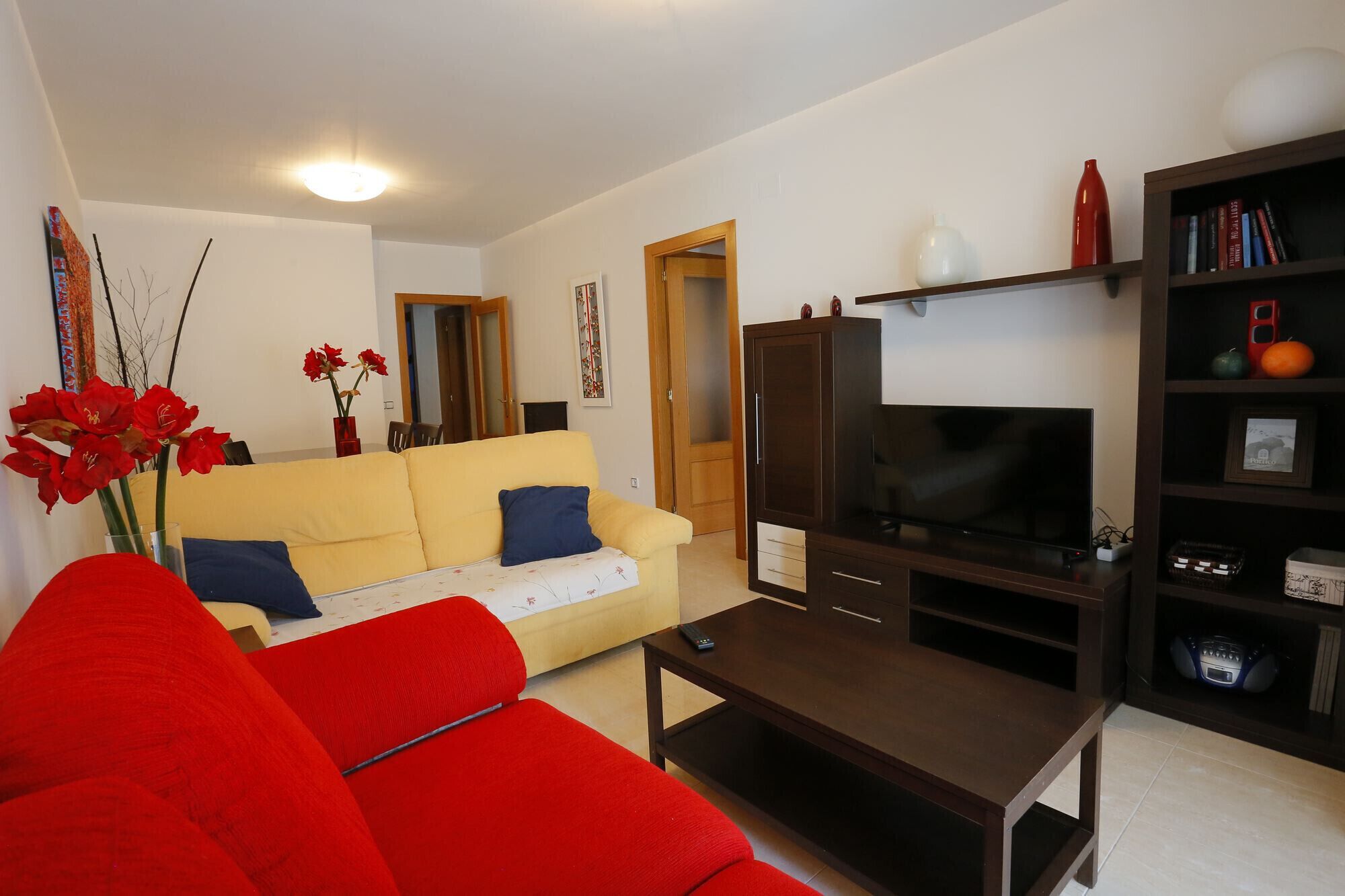 A living room with a yellow sofa, a red sofa, a TV, and a bookshelf.
