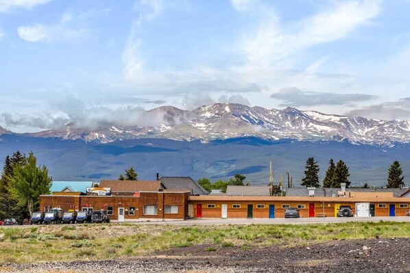Un edificio con una fila de habitaciones, un estacionamiento y vistas a montañas nevadas.