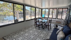 A spacious room with large windows, a patterned rug, a blue sofa with cushions, and a dining table with chairs.