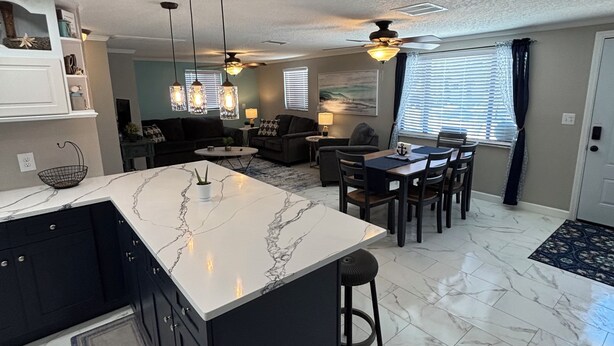 A modern kitchen with a marble island, black cabinetry, and pendant lighting.