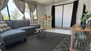 A modern living room with a grey sofa, a coffee table, and a patterned rug. There is a sliding glass door leading to a balcony.