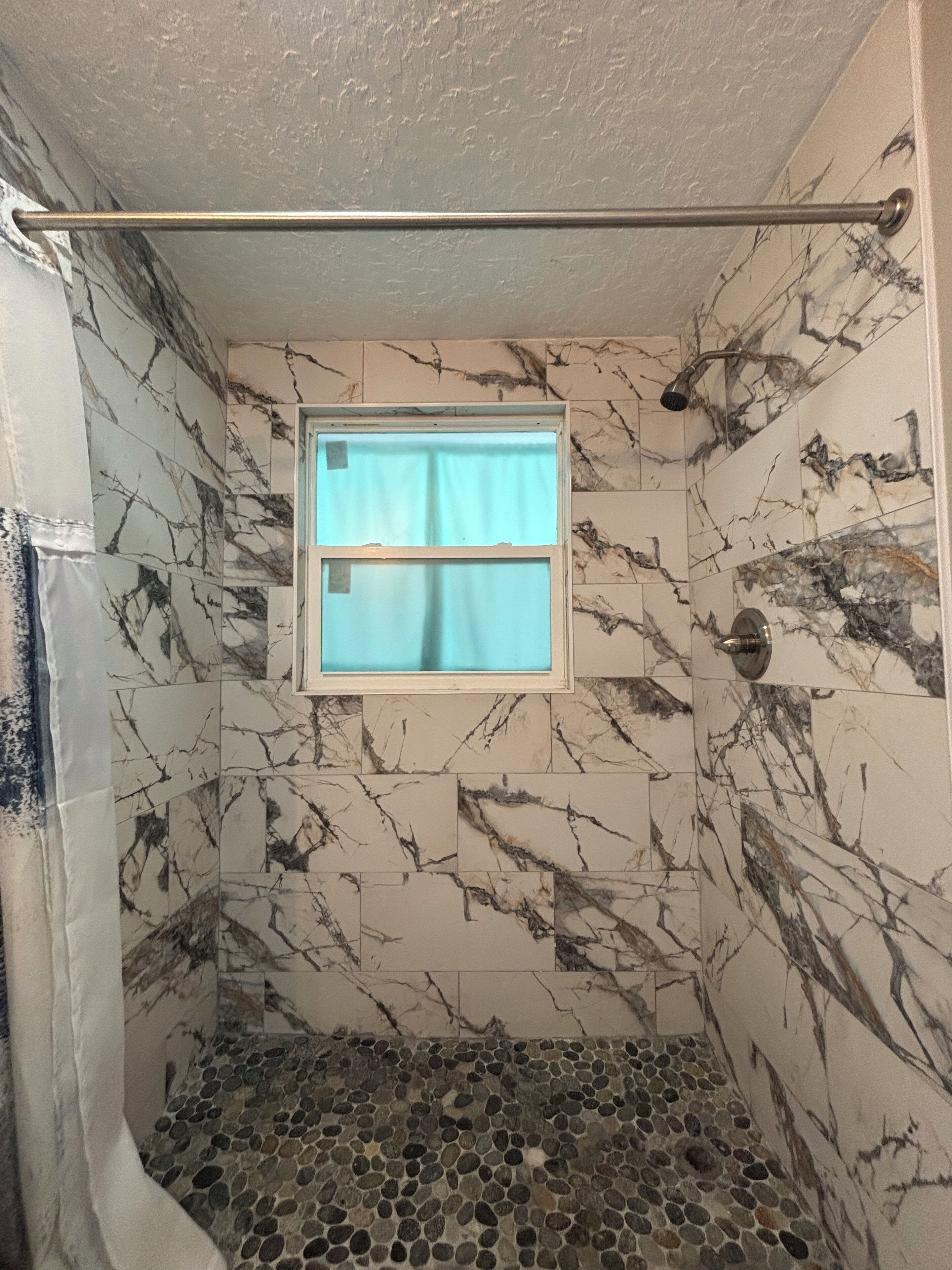 A shower with a window, marble walls, and a tiled floor.