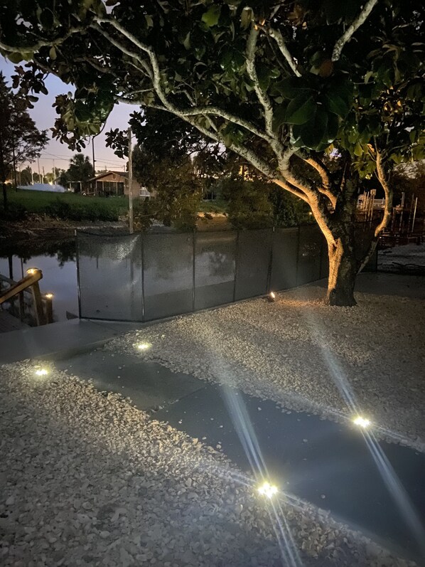 A tree-lined pathway with pebbles and a fence.