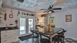 A kitchen with a black countertop, white cabinets, a ceiling fan, and a dining area with a black table and chairs. - Seminole Comfort: Private Pool Home - 3BD/2BA (Private Homes)