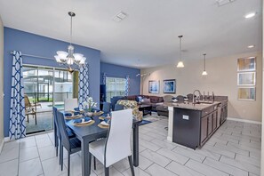 A modern kitchen with a central island, dining area with a table and chairs, and a living room with a sofa and a coffee table. - Spacious and Luxurious Home With Splash Pool, Close to Disney #4st804 (Kissimmee)