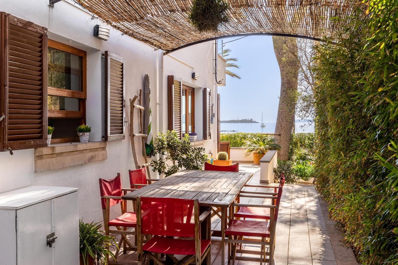 Eine Terrasse mit einem Holztisch und roten Stühlen, mit Blick auf ein Gewässer.