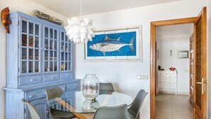 A dining area with a round glass table, grey chairs, a blue cabinet, and a framed fish painting on the wall. - Beautiful, 3 bedroom, ground floor, sea front property, large furnished terrace (Puerto de Pollensa)