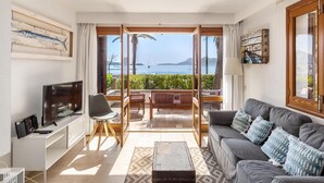 A living room with a sofa, TV, and a balcony with a view of the sea. - Beautiful, 3 bedroom, ground floor, sea front property, large furnished terrace (Puerto de Pollensa)