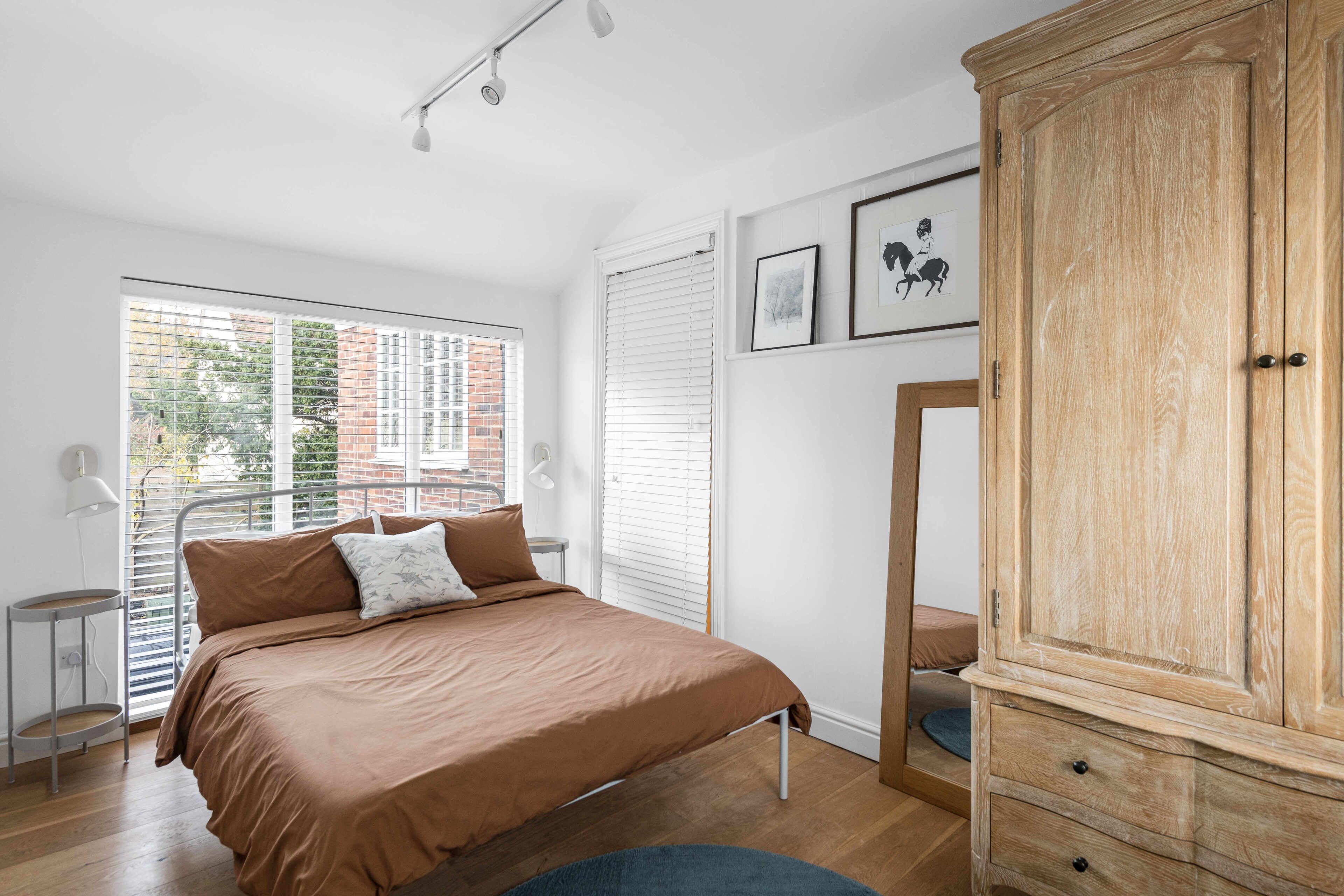 A bedroom with a bed, a wardrobe, a window with blinds, and a small table.