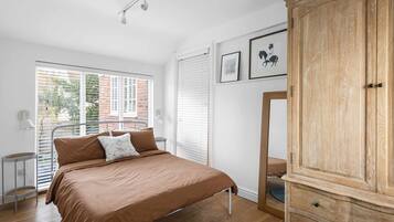 A bedroom with a bed, a wardrobe, a window with blinds, and a small table.