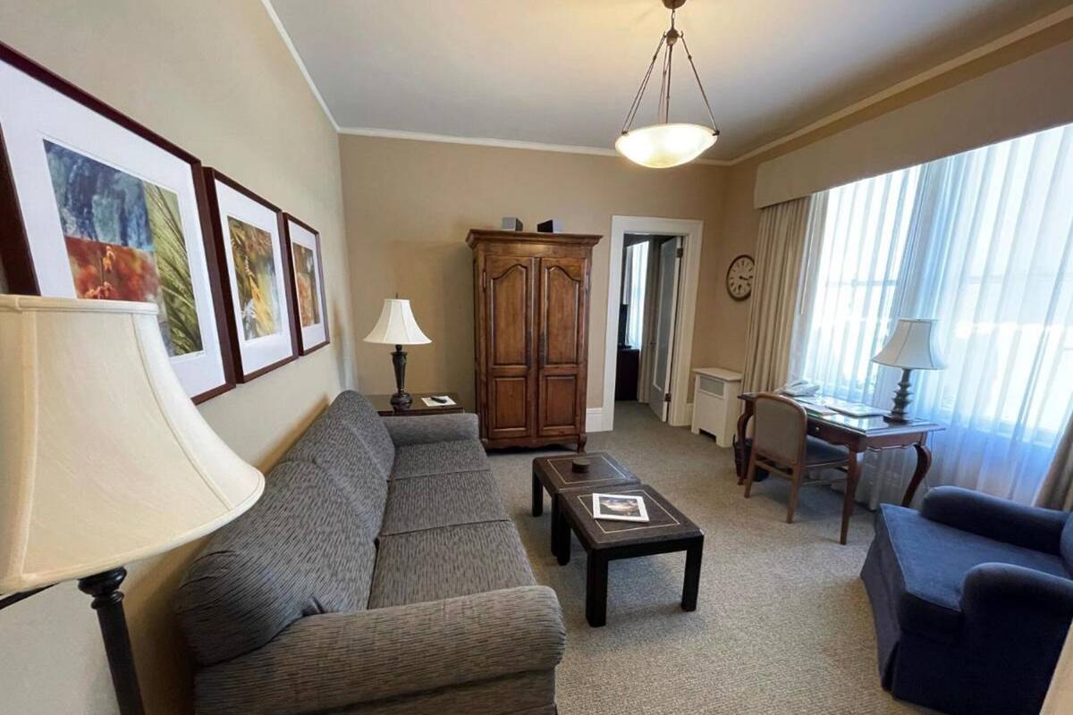 Un salon comprenant un canapé, un fauteuil, une table basse et un meuble en bois. On y trouve des tableaux encadrés accrochés au mur, une lampe et une horloge.