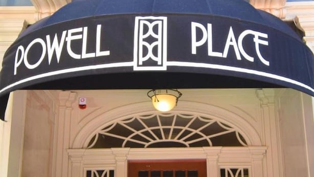 The entrance to Powell Place with a black awning, a red door, and two potted plants on either side. - Powell Place at Nob Hill (San Francisco)
