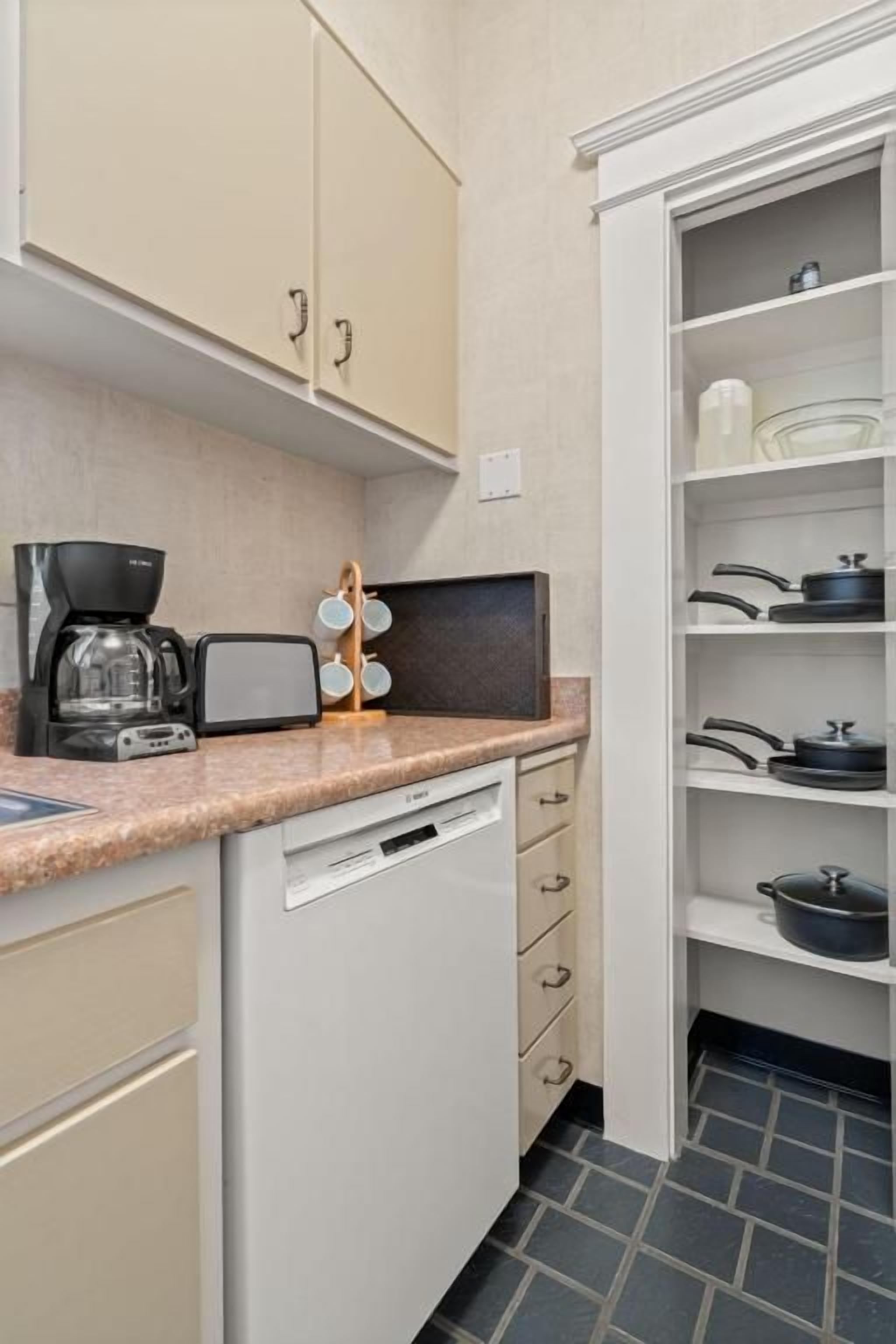 Eine kleine Küche mit Kaffeemaschine, Toaster und Mikrowelle auf der Arbeitsplatte. Darunter befinden sich Schränke und ein Geschirrspüler.