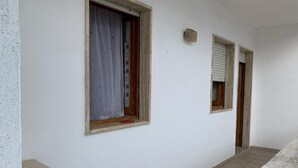 A corridor with two windows, one with a curtain and one with blinds, leading to a door. - Confortevole Appartamento Vacanza (Otranto)