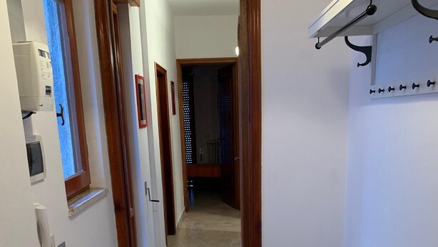 A hallway with a wooden door frame, a white bench, and a wall-mounted shelf with hooks. - Confortevole Appartamento Vacanza (Otranto)
