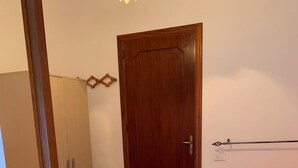 A bedroom with two beds, a wardrobe, a door, and a nightstand with a lamp. - Confortevole Appartamento Vacanza (Otranto)