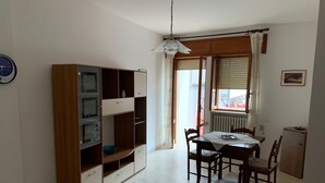 A dining area with a wooden table and chairs, a cabinet with glass doors, and a window with curtains. - Confortevole Appartamento Vacanza (Otranto)
