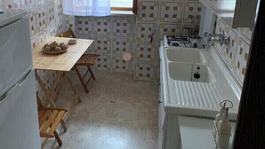 A compact kitchen with a wooden table, a sink, and a refrigerator. - Confortevole Appartamento Vacanza (Otranto)