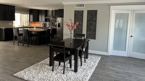 A modern kitchen with dark cabinetry, a central island, and a dining area with a white rug and dark chairs. - Resort Living near Kierland and Mayo Clinic  (Scottsdale)
