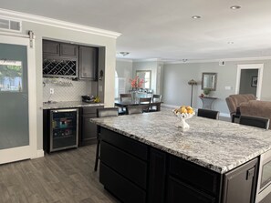 A modern kitchen with dark cabinetry, a marble island, and a dining area with a chair and table.