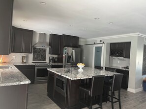 A modern kitchen with dark cabinetry, granite countertops, stainless steel appliances, and a central island with bar stools.