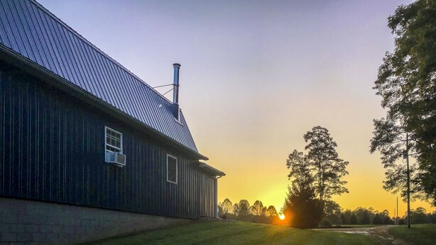 Puinen rakennus, jossa on metallikatto ja savupiippu, ja sen ympärillä on nurmikkoa ja puita.