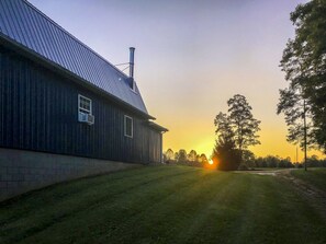 A wooden building with a metal roof and a chimney, surrounded by grass and trees. - "The Barn at Sunset Lane" - Spacious 4BR Home on 16 Acres (Killbuck)